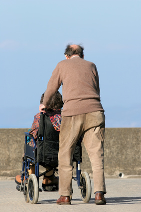Rear View Oif An Elderly Man Pushing An Elderly Female In A Wheelchair On A Pavement With A Blue Sky To The Rear. - Pushing Wheelchair, Transparent background PNG HD thumbnail